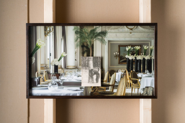 A visual art work by Vietnamese-Canadian artist Phuong Ngo from his series Lost and Found. A high resolution print of a luxury restaurant interior, a postcard in black and white glued on top of it. The postcard shows a young person harvesting rubber from a tree in French colonial Vietnam.